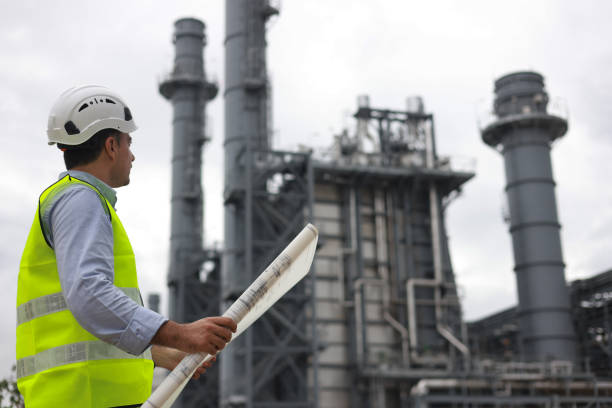 Electrical engineers, holding blueprints, look confident at the thermal power plant while working on project planning to produce high-voltage electrical energy, emphasizing the energy concept.